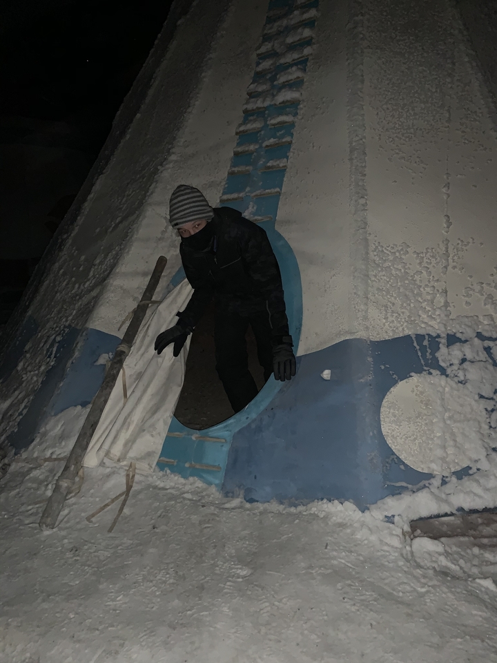 Person peeking out from a snow-covered teepee entrance.
