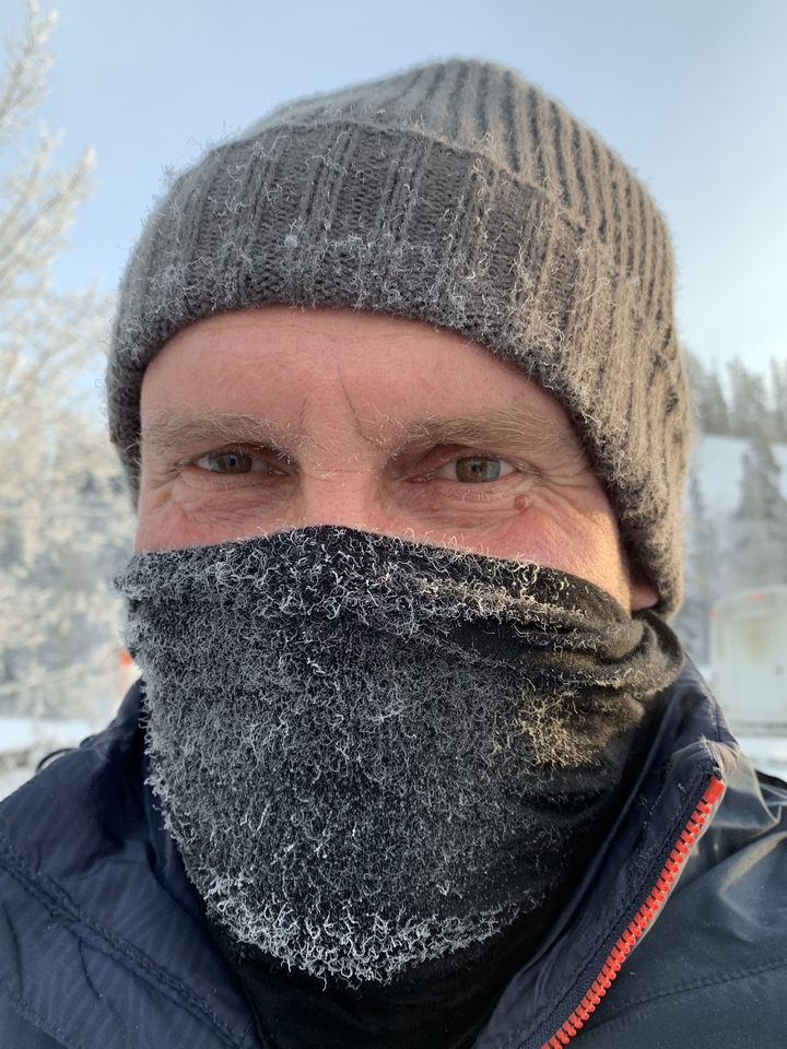 Close-up of a person wearing a winter hat and face covering, with frost on the fabric.