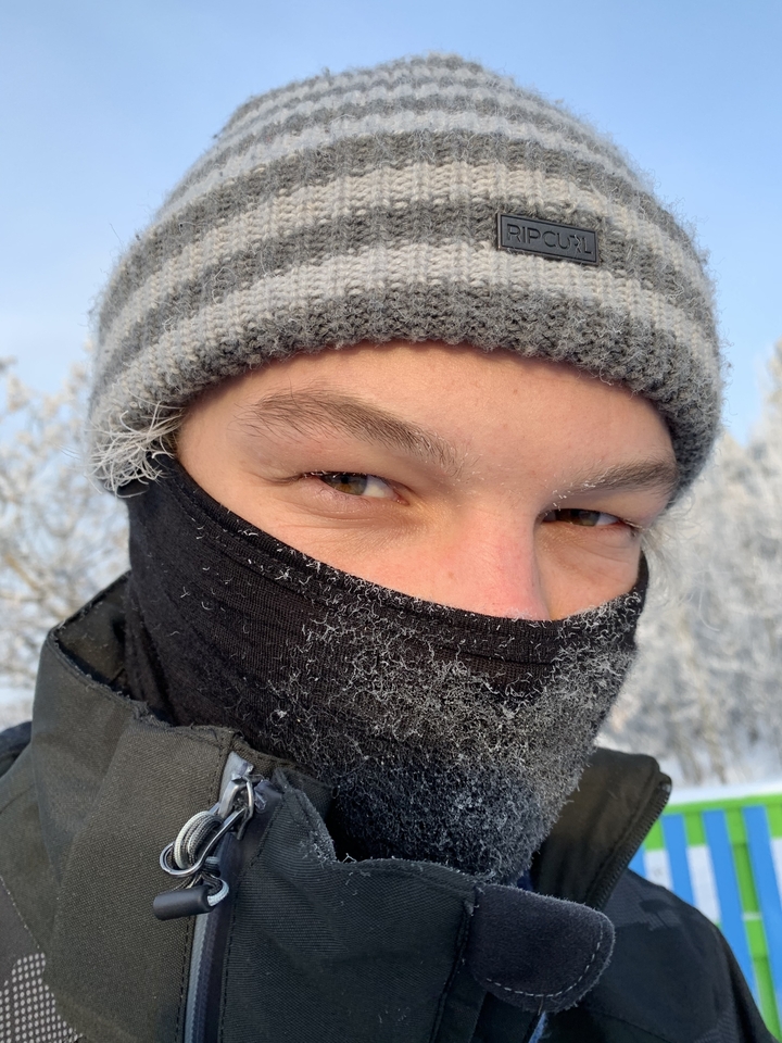 Close-up of a person's face wearing a face covering and winter hat, with frost.