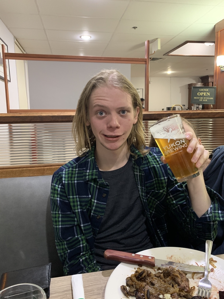 A person holding a pint of Yukon Brewing beer inside a restaurant.