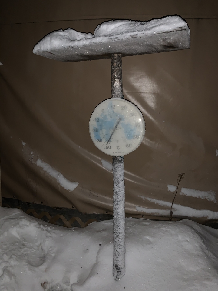 A frosty thermometer against a wall, showing negative temperatures.