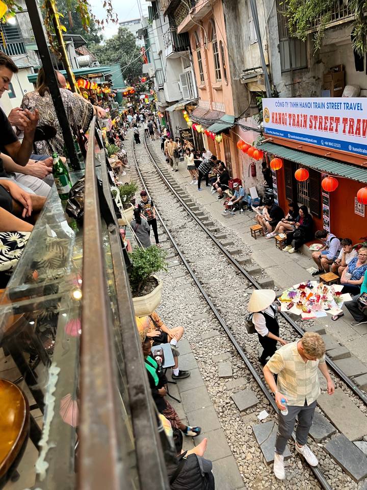 Rue marchande animée le long des voies ferrées bordée de gens et de boutiques.