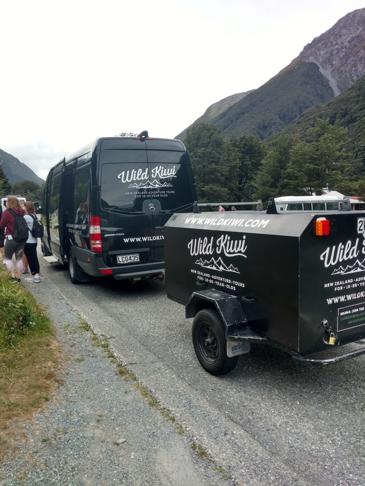 A tour van with people standing nearby at a scenic roadside.