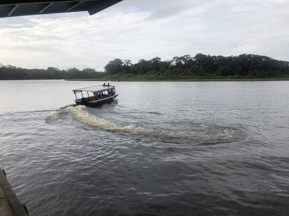 A boat creating wake as it moves through a river surrounded by lush vegetation.