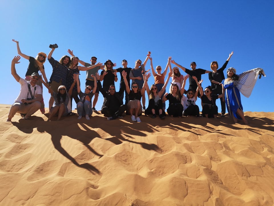 Group of people posing with arms raised in the desert.