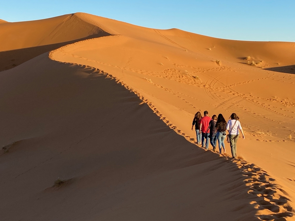 People walking along sand dunes at sunset.