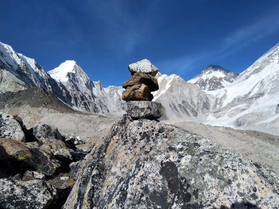 Stones balanced in front of snowy mountain peaks under a clear blue sky.