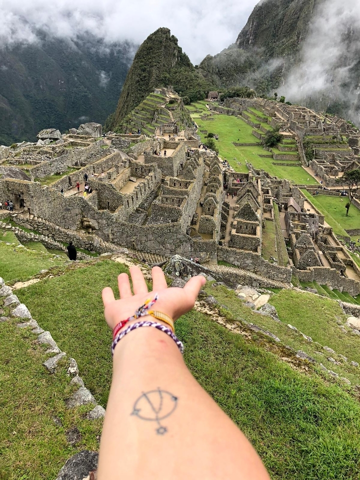 Hand pointing towards Machu Picchu ruins.