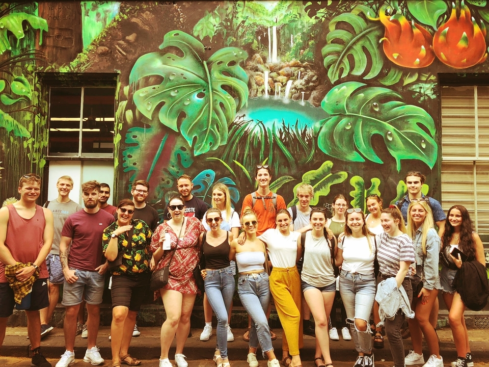 Group posing in front of a colorful mural in an urban setting.