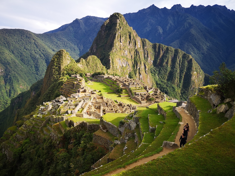View of Machu Picchu from an elevated angle with tourists walking.
