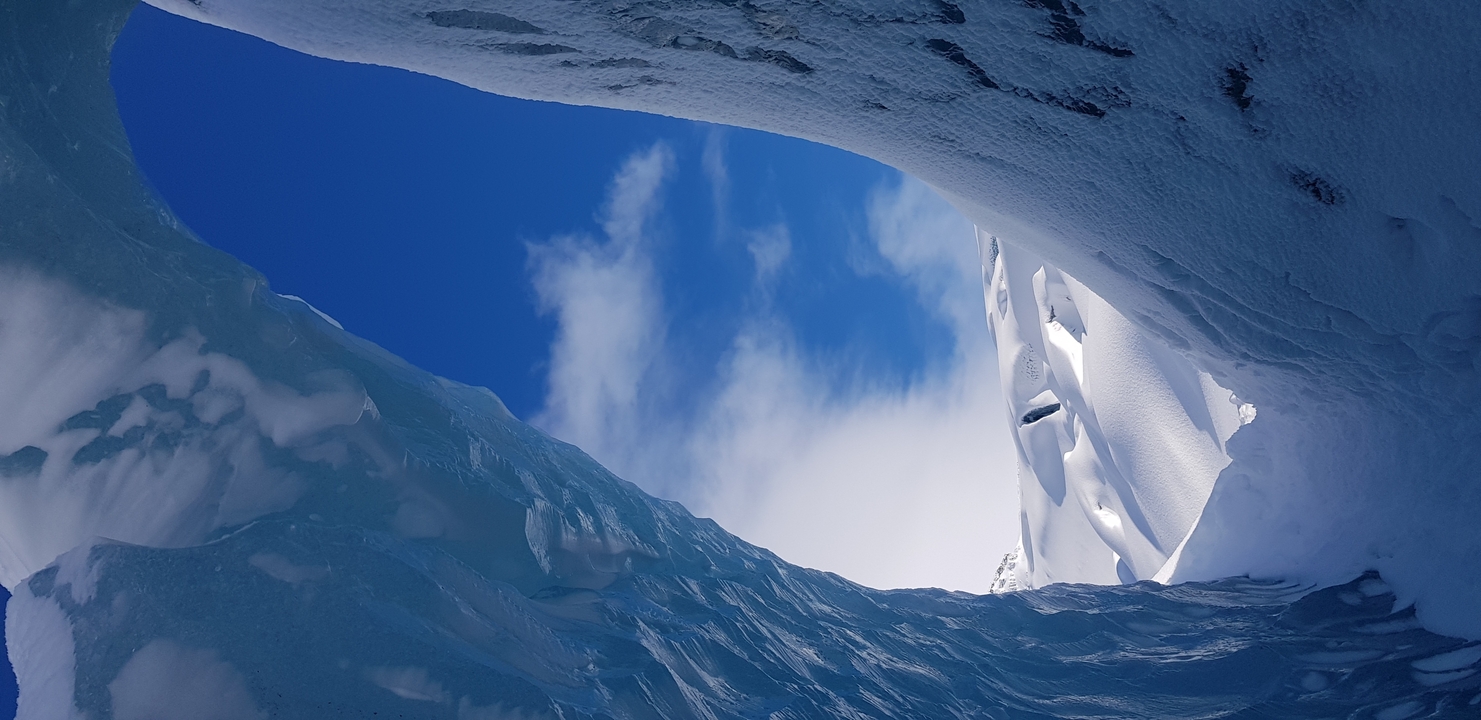 View from inside a blue ice cave looking out to the sky.