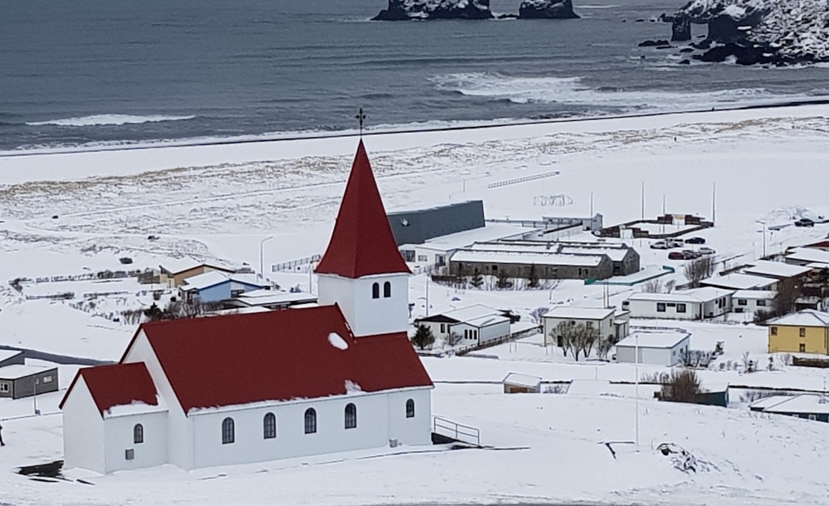 Scenic view of a red-roofed church in a snowy village near the ocean.