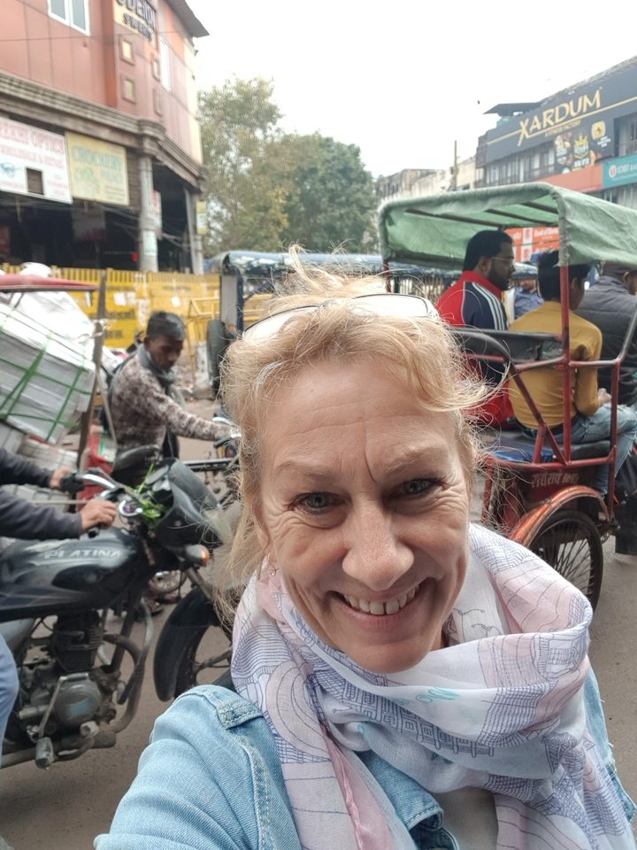 Person smiling in a street filled with rickshaws and people.
