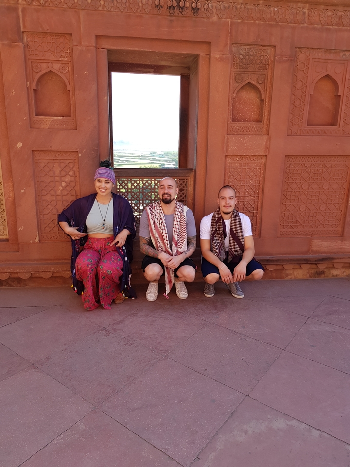 Three people sitting and posing in front of ornate wall.