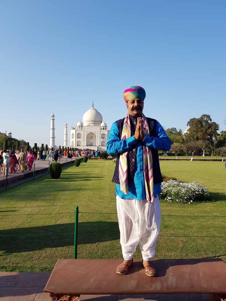 Man posing in traditional attire in front of the Taj Mahal.