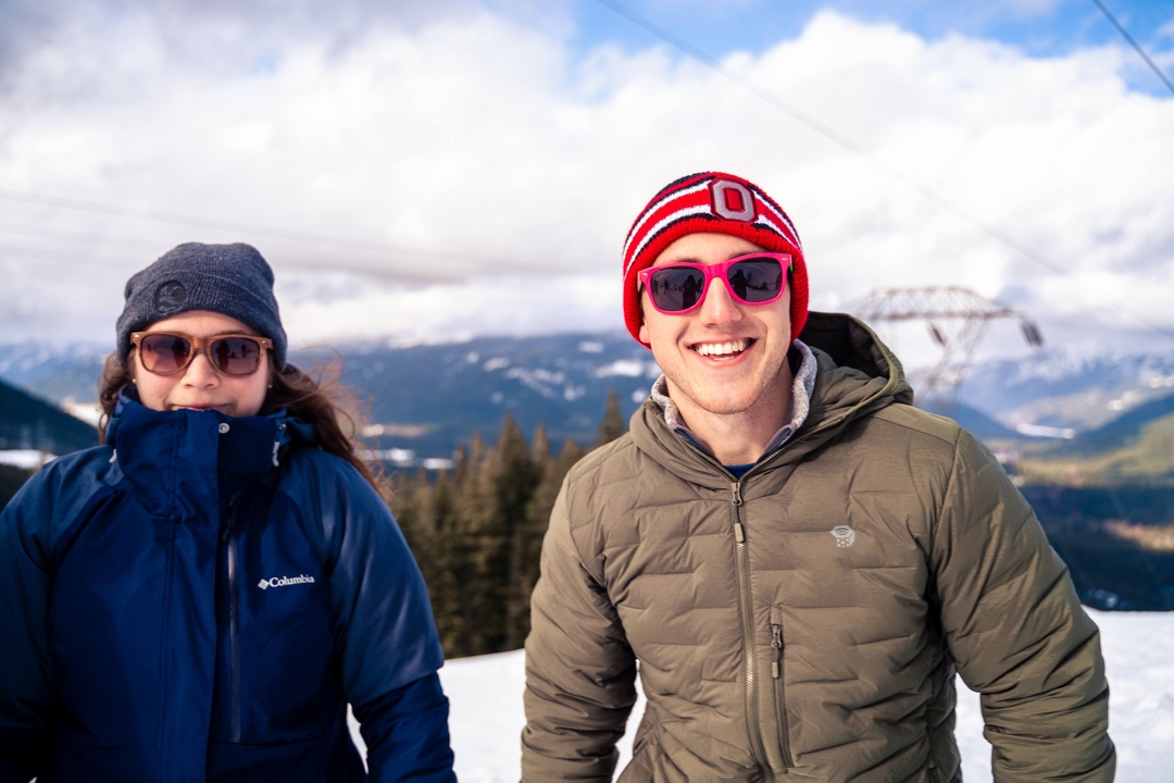 Two people in winter gear posing in snowy mountains.