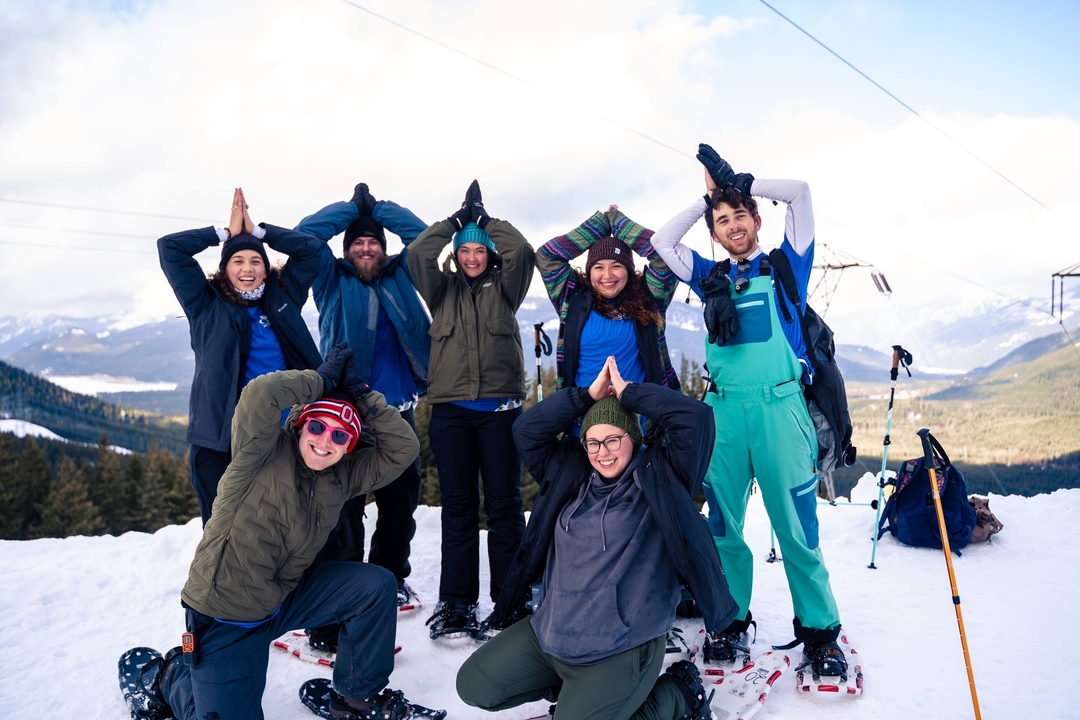 Group of people making poses in the snow with mountains in the background.