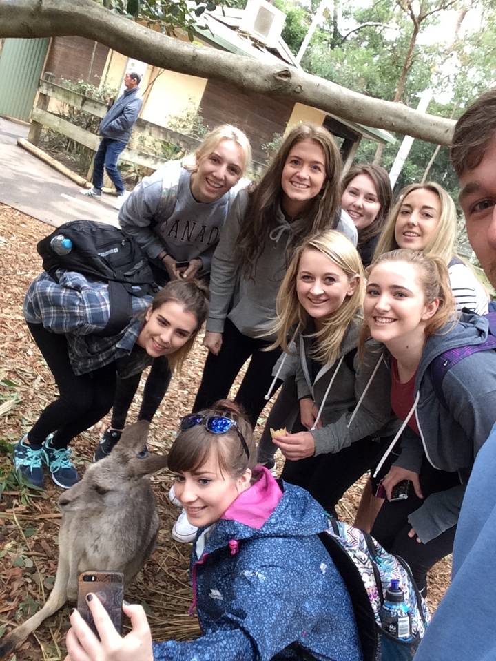 Group of people posing with a kangaroo in a natural setting.
