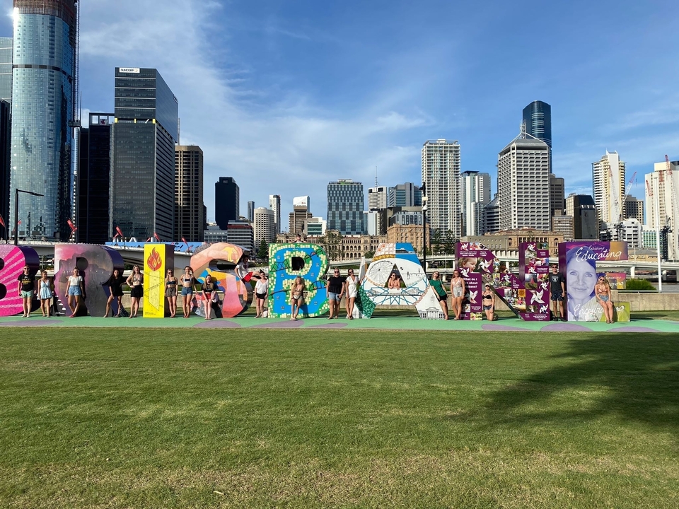 People posing in front of the Brisbane sign with city skyscrapers in the background.