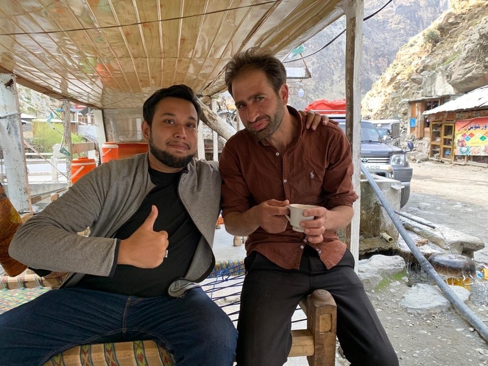 Two men sitting outdoors with a scenic mountain backdrop.