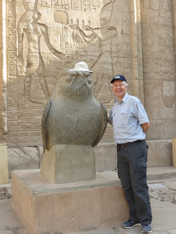 Smiling man next to a Horus statue at an Egyptian site.