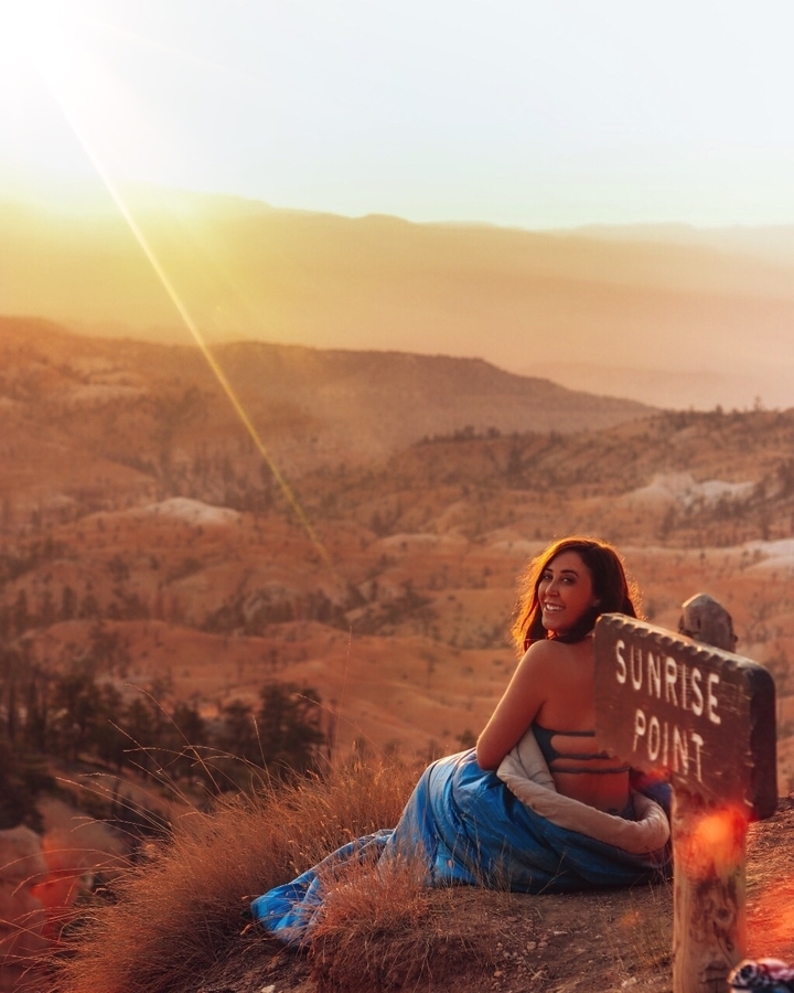 Woman smiling at sunrise with mountainous landscape.