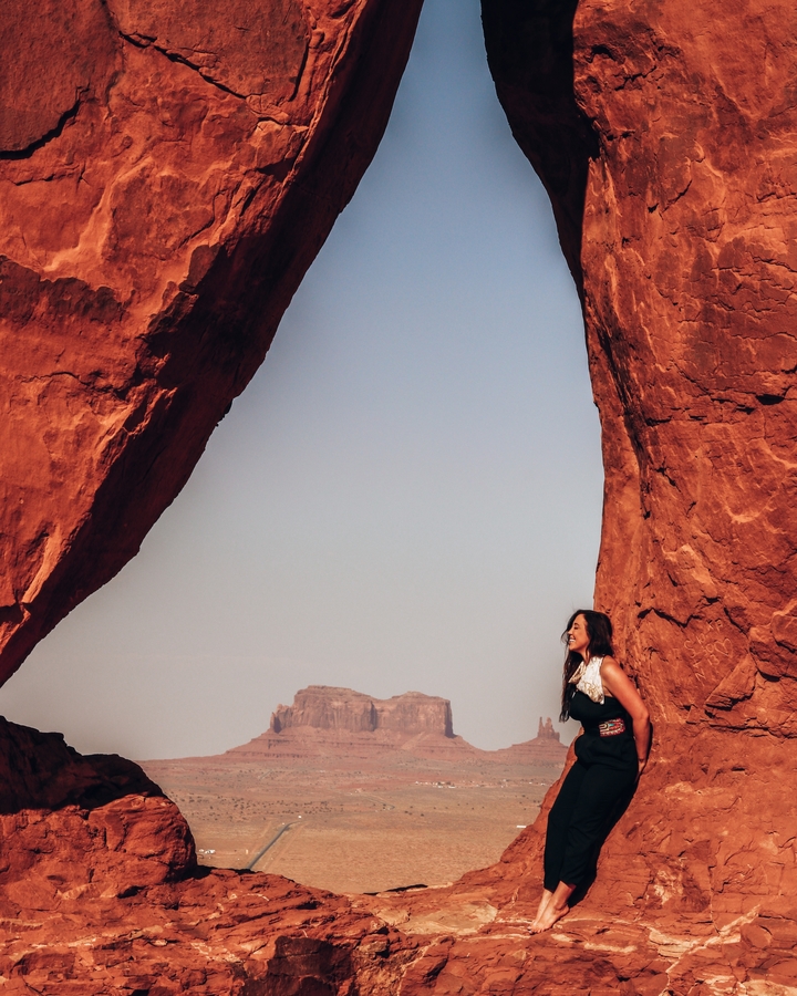 Person standing under a large rock arch with a view.