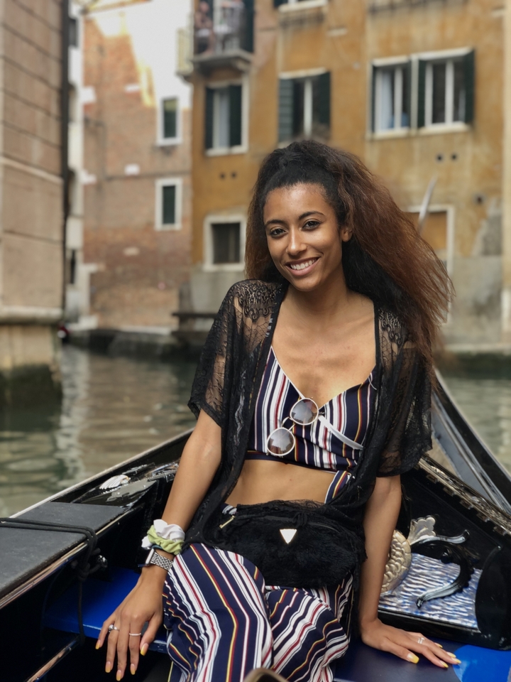 Smiling woman sitting on a gondola in a Venetian canal.