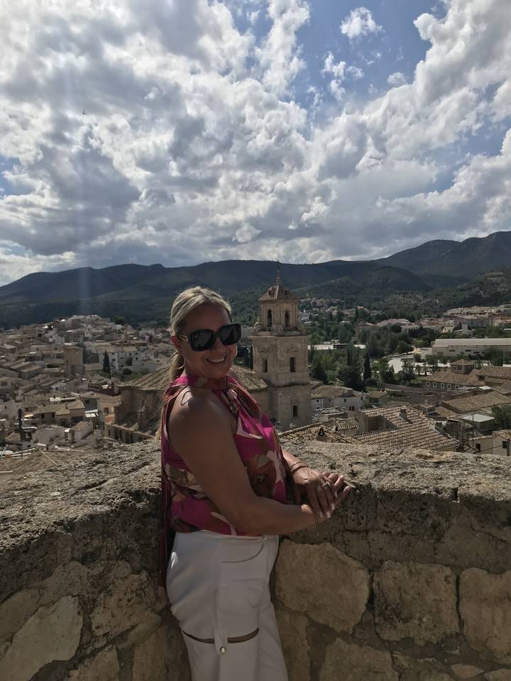 A smiling woman posing on a stone wall with a town in the background.