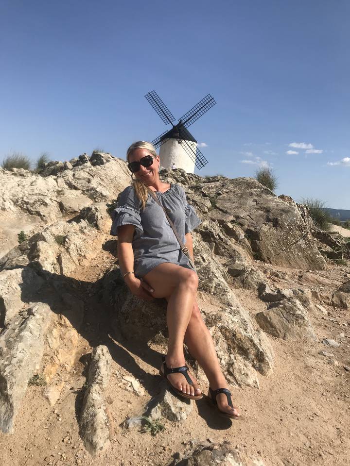 A woman sitting by a rocky outcrop with a windmill in the background.