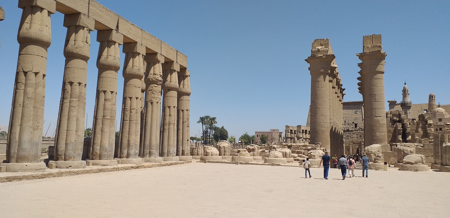 Visitors walking in front of large temple ruins in Luxor.