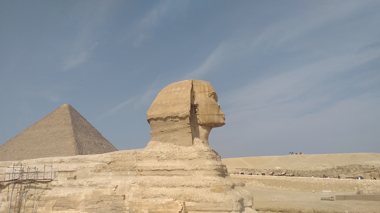 Side view of the Sphinx with a pyramid in the background.