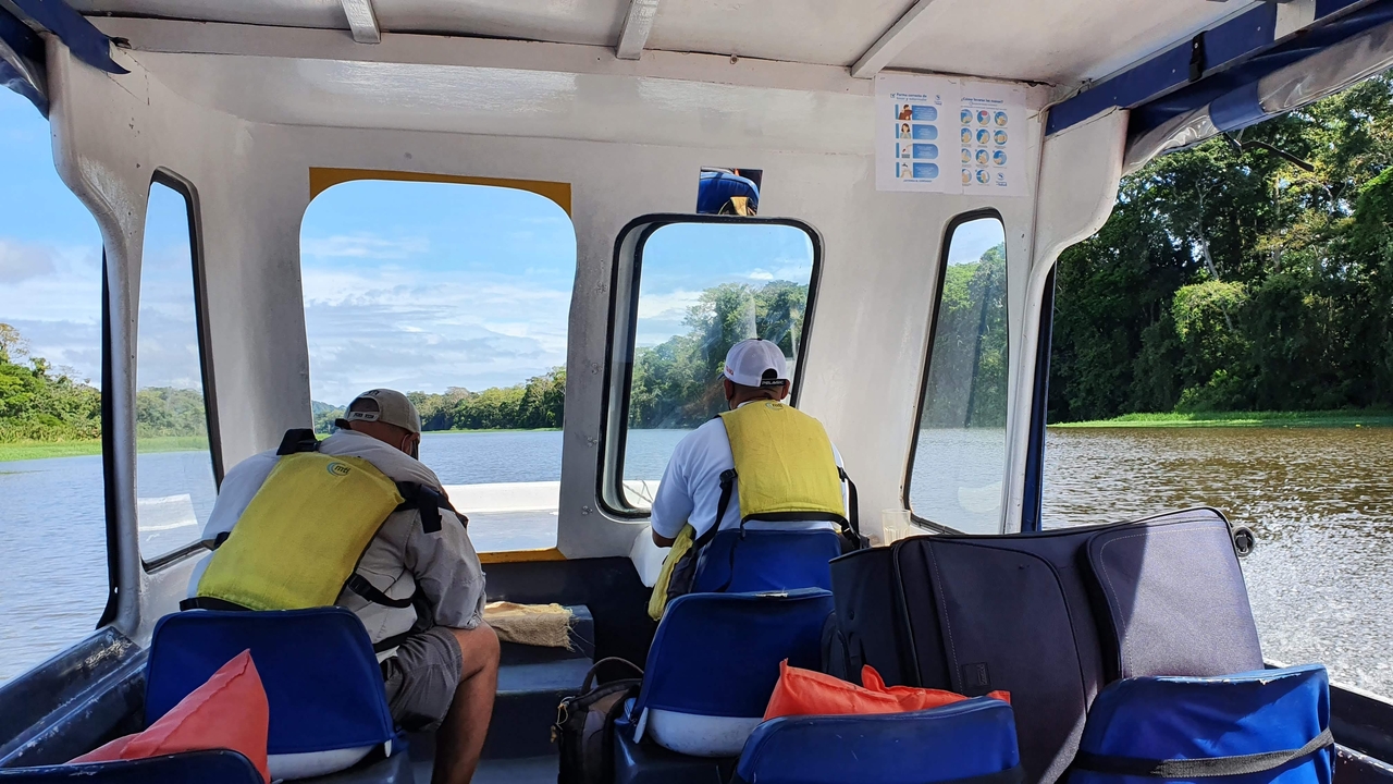 Two people on a boat in a river surrounded by jungle.