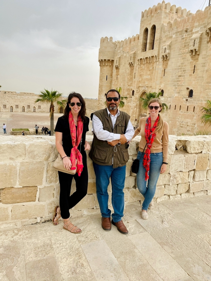 Three people standing on a stone wall with historic buildings in the background.