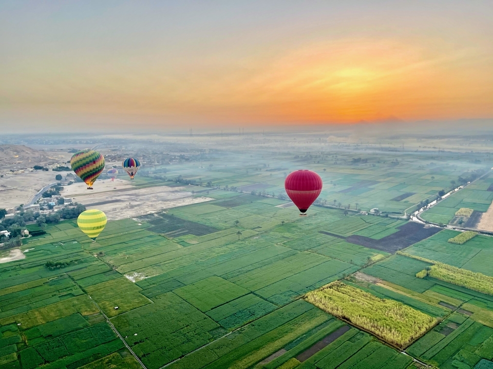 Hot air balloons floating over a lush green landscape at sunrise.
