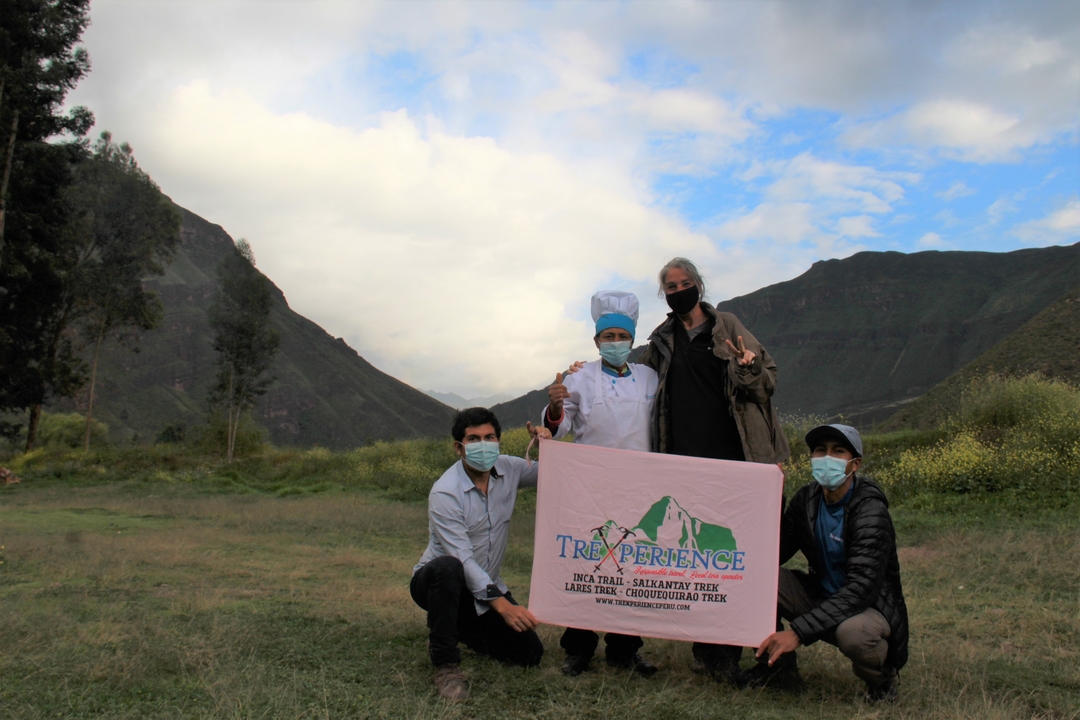 Group of people in a mountainous green landscape holding a banner.