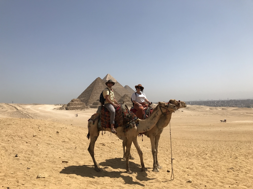 Deux personnes sur des chameaux devant des pyramides.