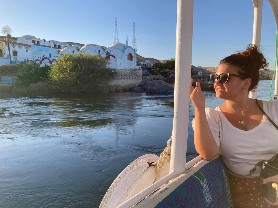 Femme sur un bateau dans une rivière avec des bâtiments colorés sur la berge.