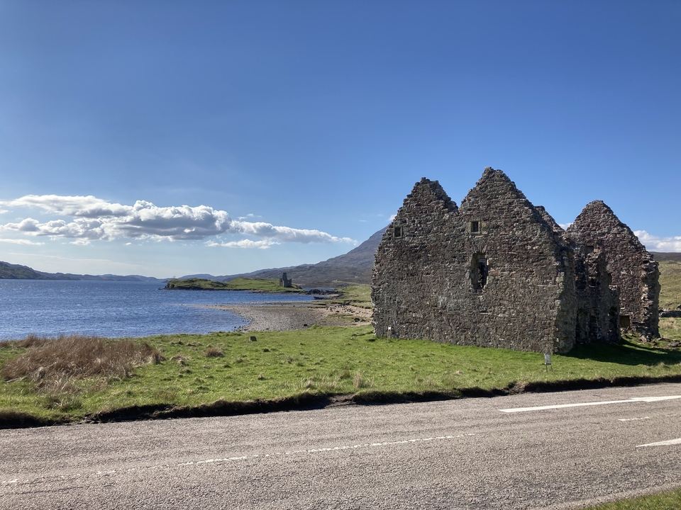 Ruines d'un bâtiment en pierre au bord d'un lac avec des montagnes en arrière-plan.