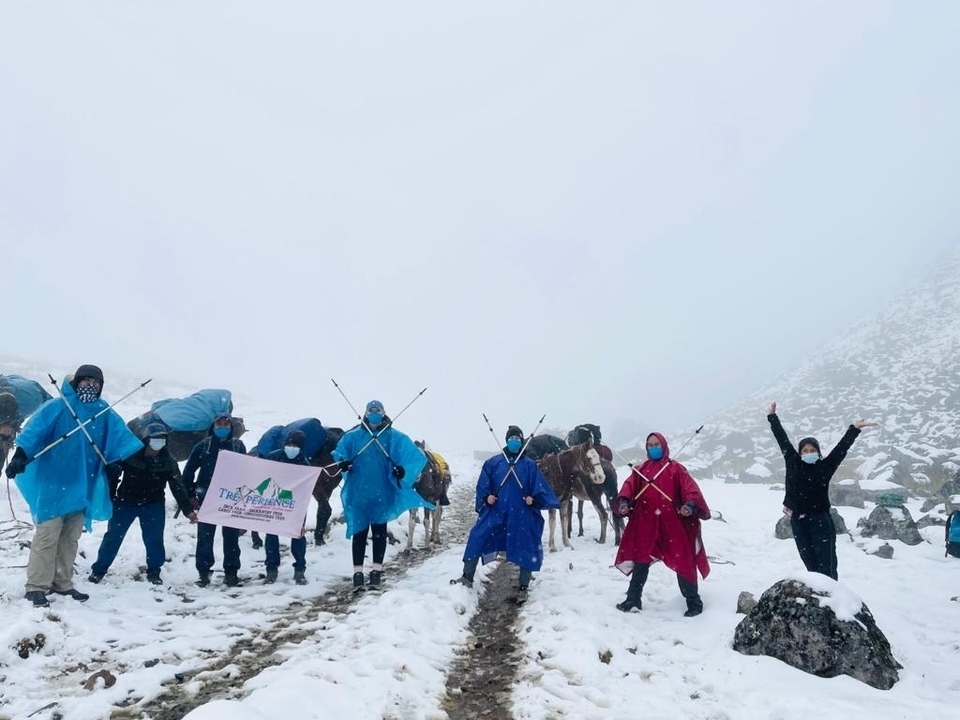 Group of hikers standing in snow holding a banner, looking triumphant.