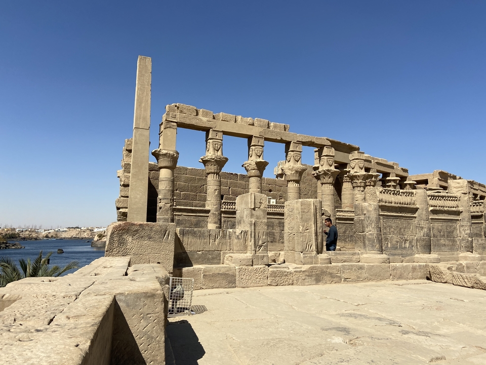 Visitor stands among the riverside columns of Kom Ombo Temple with blue waters stretching into the distance.