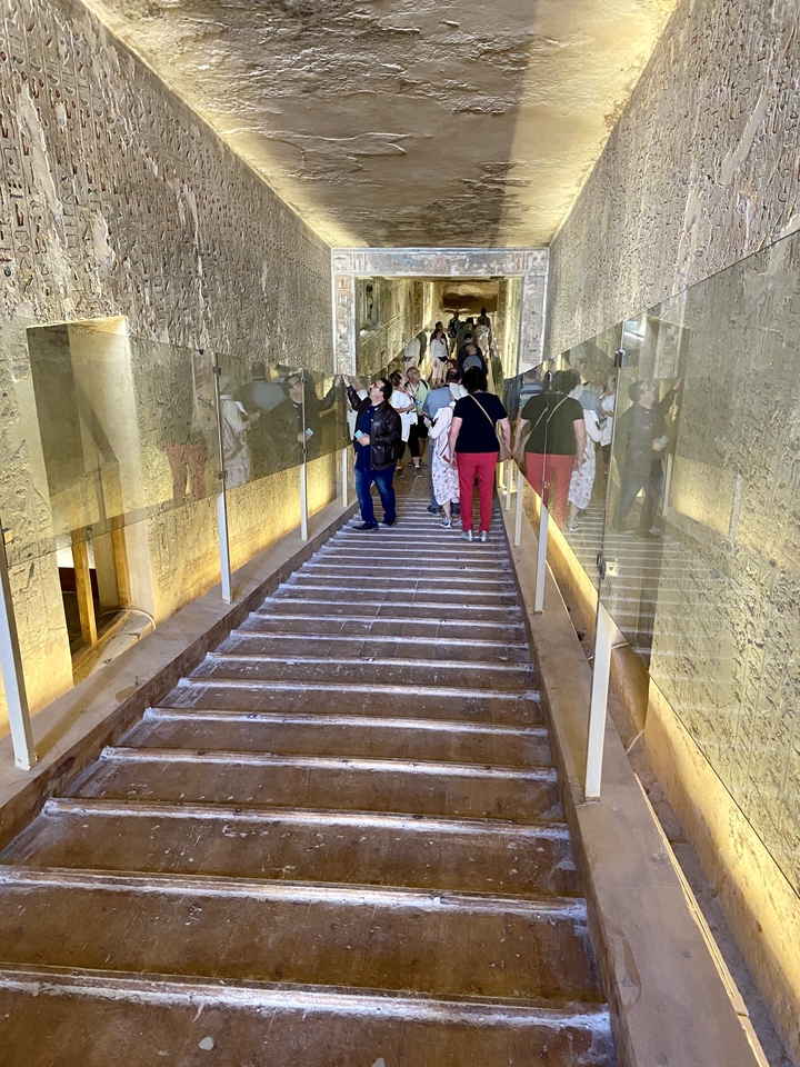 Tourists descend a staircase lined with glass panels inside a hieroglyph-covered tomb in the Valley of the Kings.