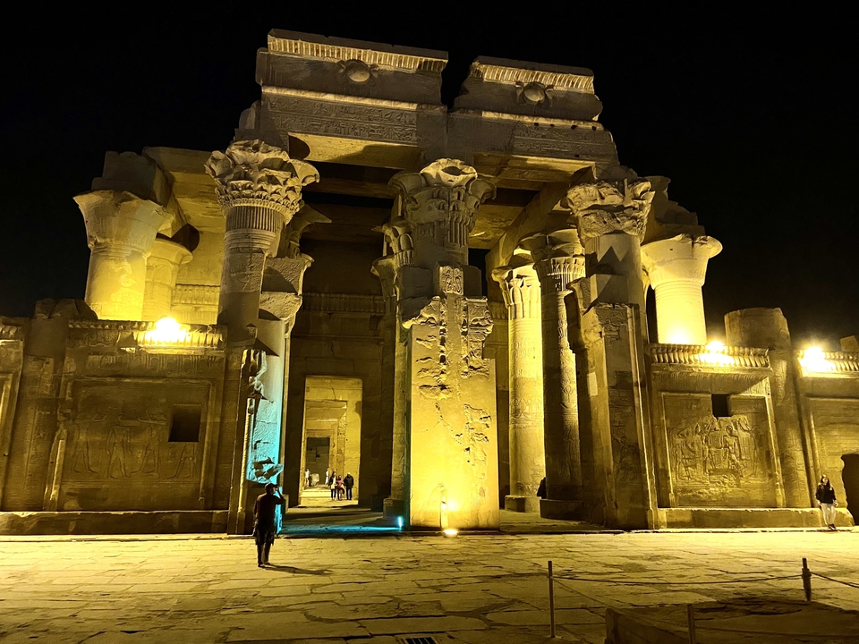 Nighttime illumination bathes the grand columns and reliefs of Kom Ombo Temple in golden and blue light.