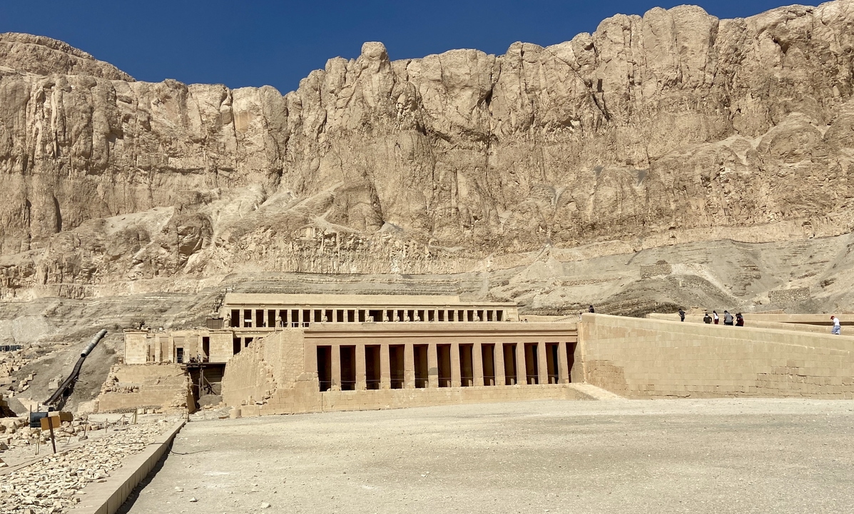 Wide view of Hatshepsut Temple nestled against towering desert cliffs under a cloudless blue sky.