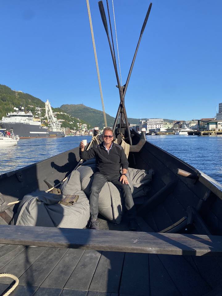 Person sitting on a wooden boat with mountains in the background.