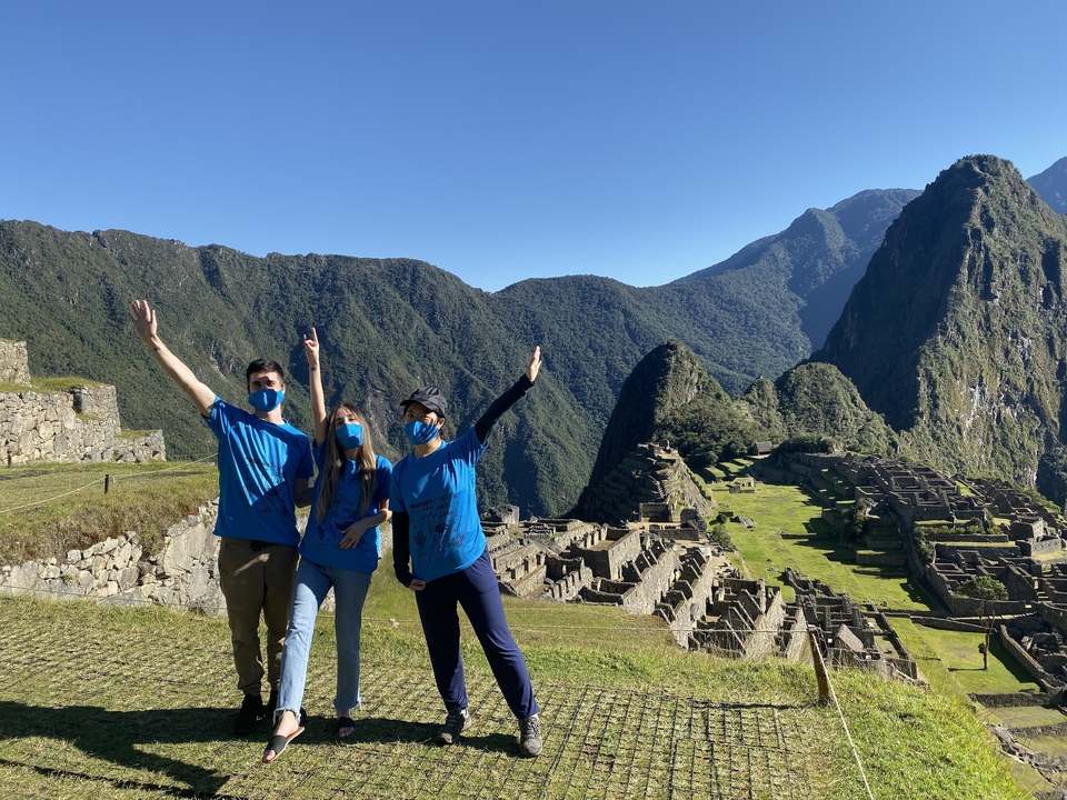 Three people in blue shirts, posing with Machu Picchu in the background.