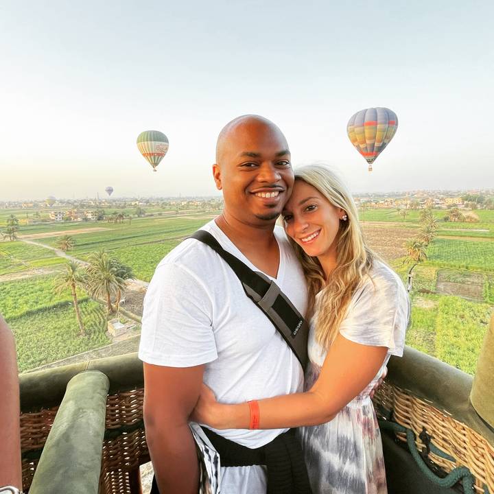 Couple in a hot air balloon basket, with other balloons around.
