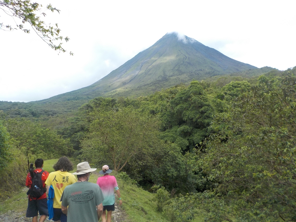 Hikers approaching the Arenal Volcano, surrounded by lush forest.