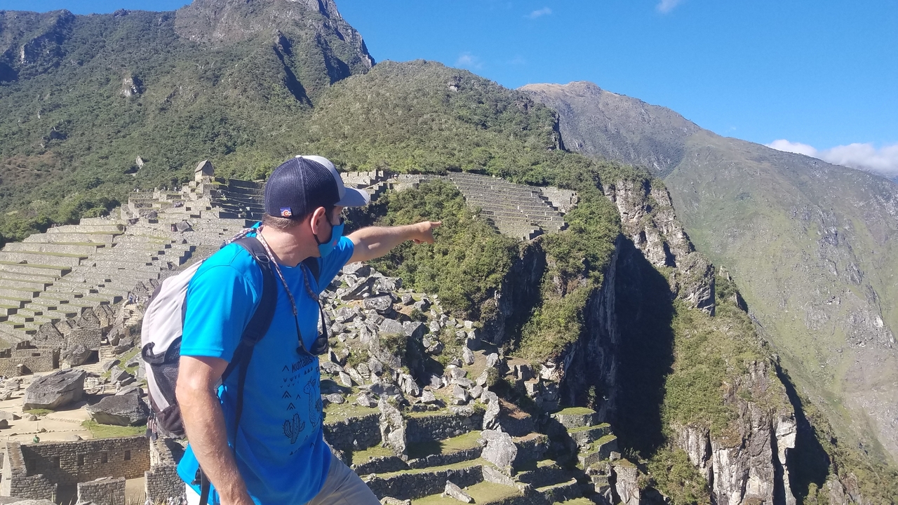 Person pointing towards ancient terraces in a mountain setting.