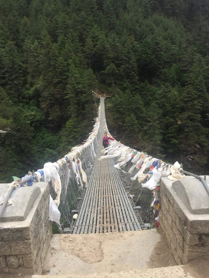 Suspension bridge with prayer flags and person crossing.
